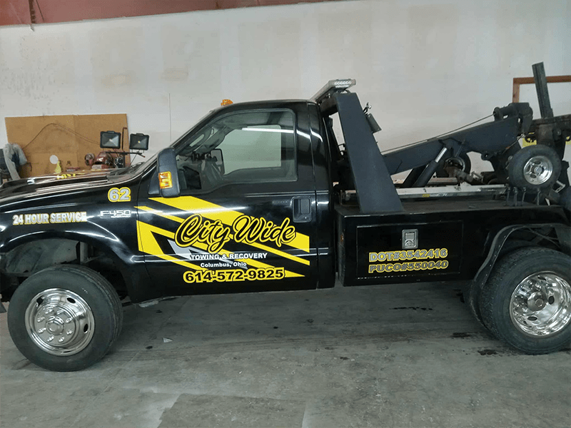 Black and yellow City Wide towing truck showcasing "24 Hour Service" and contact details