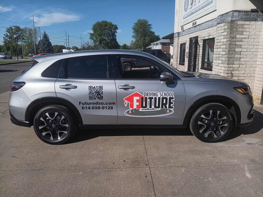 Silver SUV with a "Driving School Future" logo parked outside a building, featuring a QR code and contact information on the side.