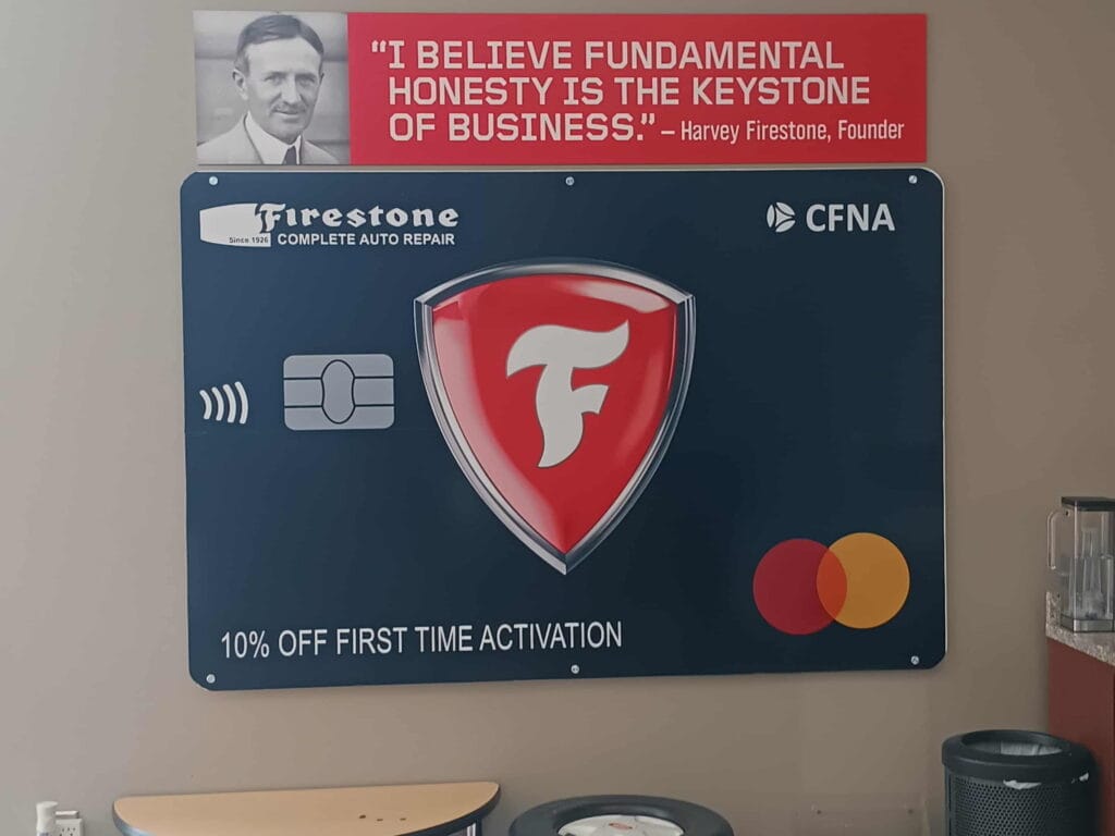 Firestone auto repair promotional sign features a quote by founder Harvey Firestone on honesty and a graphic highlighting a payment discount offer.